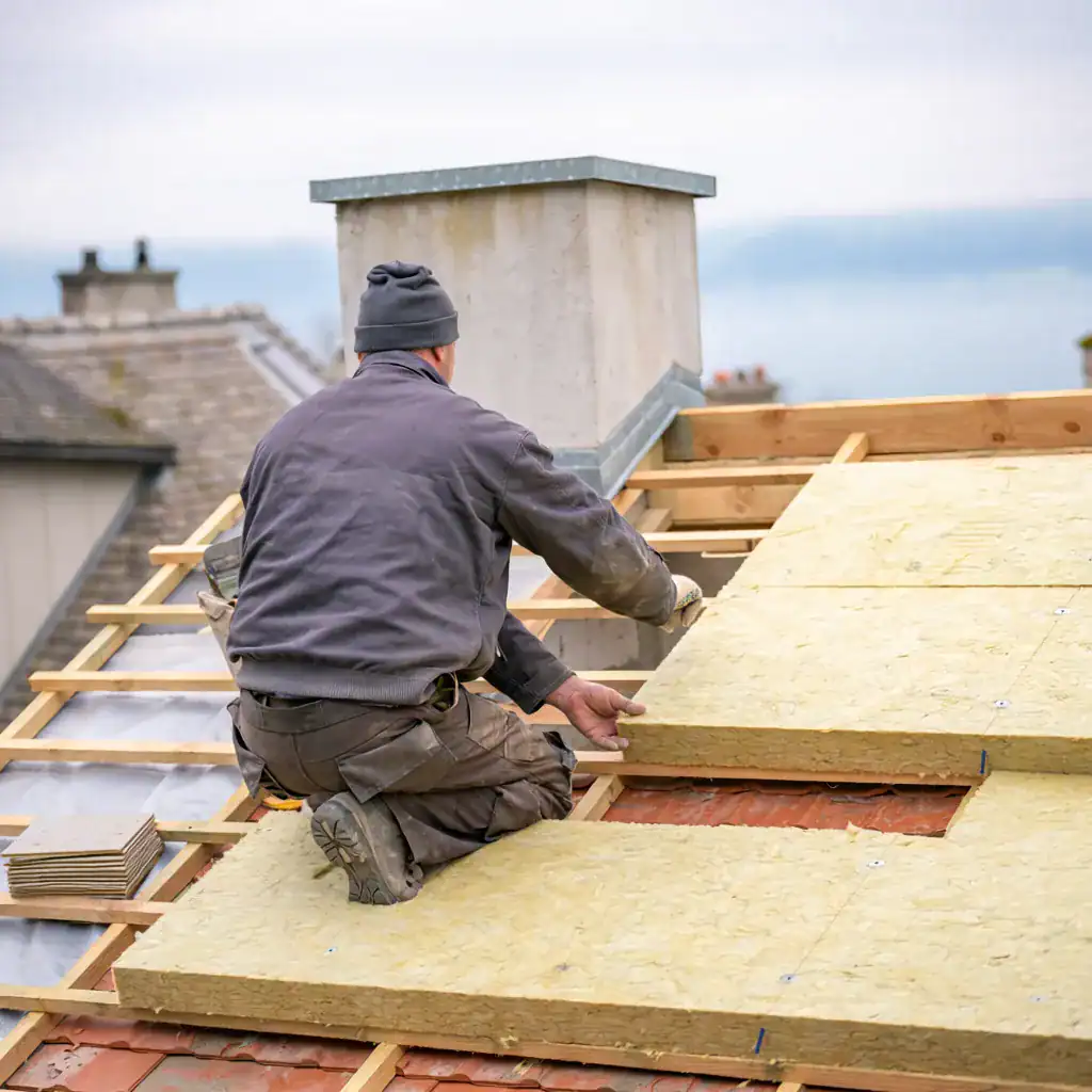 Ouvrier posant des panneaux d'isolation sur un toit en construction.